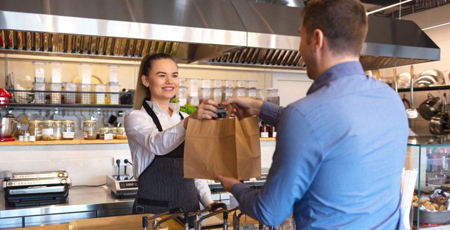 Systemgastronomie - Kellnerin übergibt einem Kunden eine Tasche